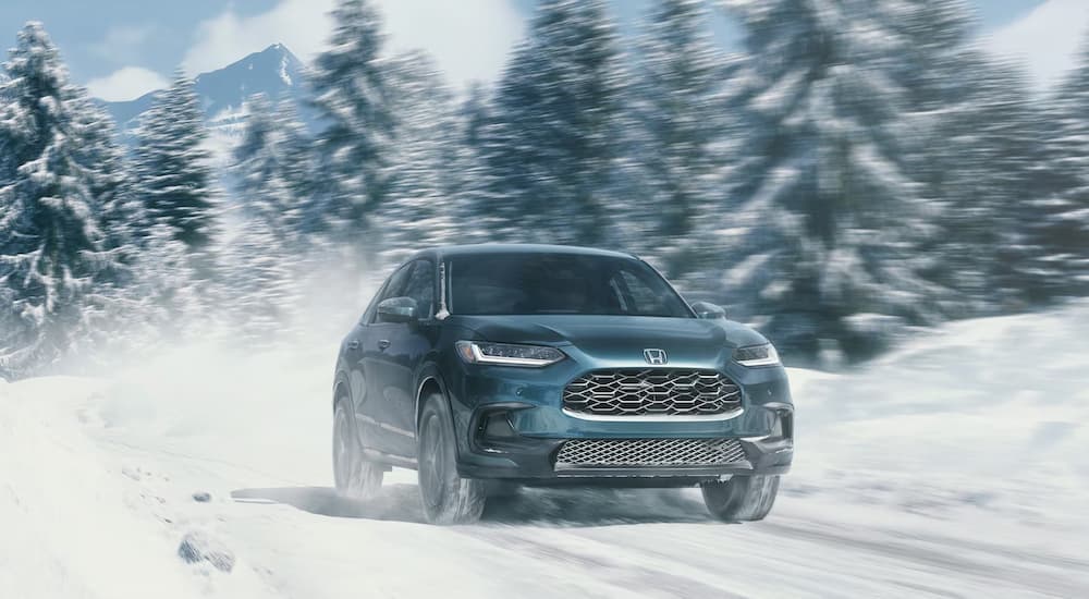 A blue 2025 Honda HR-V EX-L driving on a snowy road.