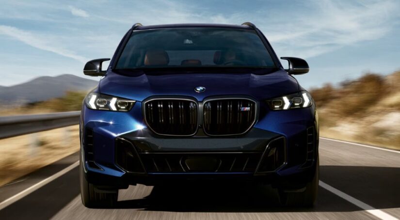 Head-on view of a blue 2025 BMW X5 M60i driving on the road.