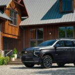 A dark grey 2025 Chevy Tahoe High Country parked in front of a rustic house.