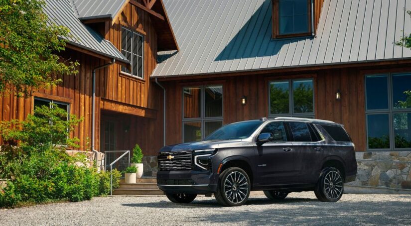 A dark grey 2025 Chevy Tahoe High Country parked in front of a rustic house.