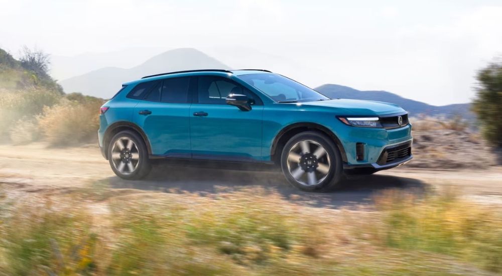 A blue 2025 Honda Prologue driving down a desert road from a local Honda dealer.