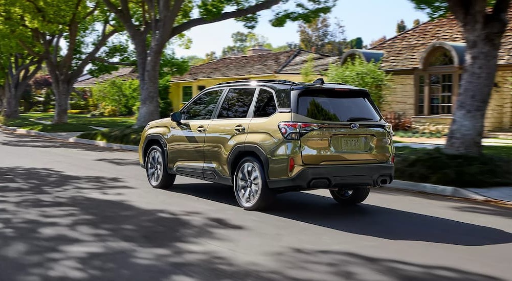 A green 2025 Subaru Forester Hybrid is shown driving in a nice neighborhood.