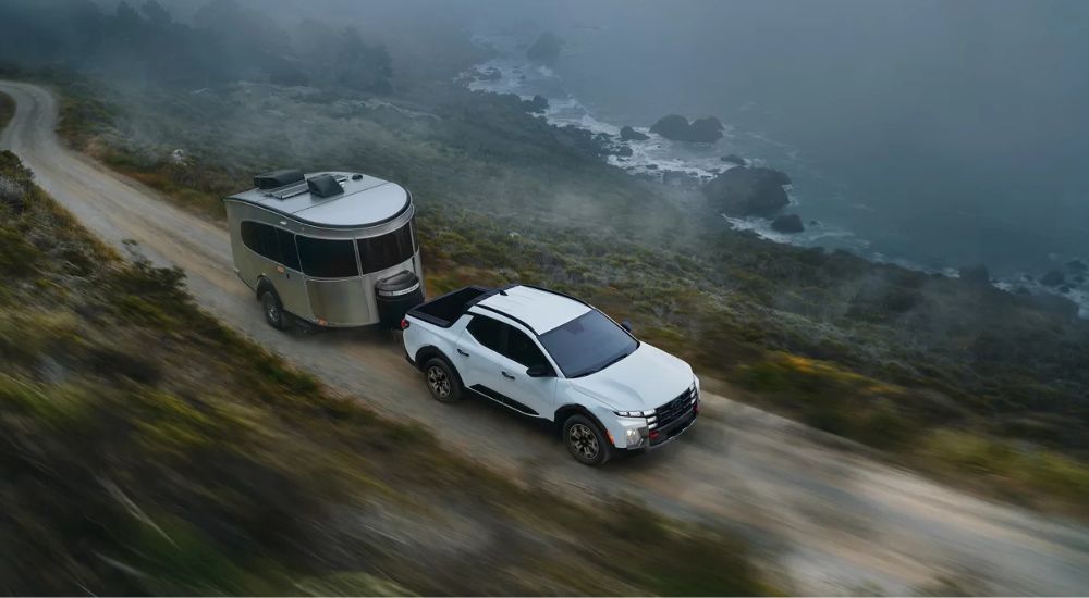 Overhead view of a white 2025 Hyundai Santa Cruz XRT towing a trailer along a coastal dirt road.