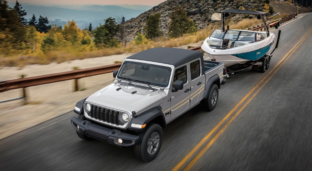 A silver 2025 Jeep Gladiator Sport S is shown towing a boat.