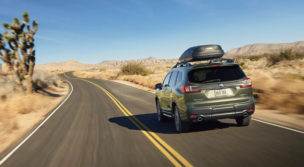 A green 2025 Subaru Ascent is shown from the rear on an open road.