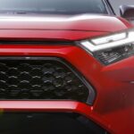 A close-up on the headlight and grille of a red 2025 Toyota RAV4 Hybrid.