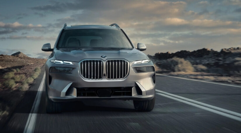 A grey 2026 BMW X7 for sale is driving on a highway.