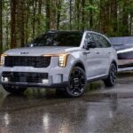 A white 2025 Kia Sorento X-Pro SX Prestige towing a boat on wet pavement.