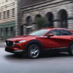 A red 2025 Mazda CX-30 driving through a city.