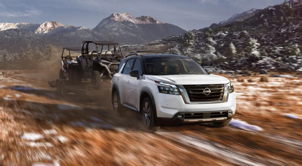 A white 2025 Nissan Pathfinder towing ATVs.