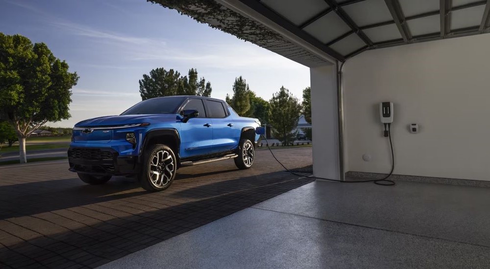 A blue 2024 Chevy Silverado EV RST plugged into a garage