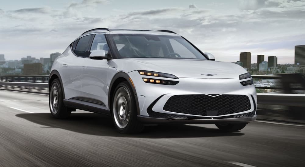 A white 2025 Genesis GV60 driving on a highway.