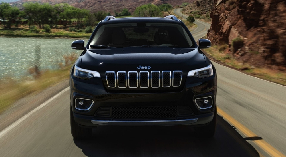 A black 2021 Jeep Cherokee driving past a lake.