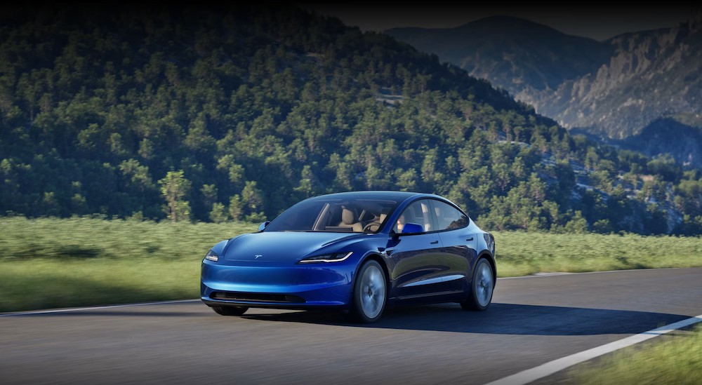 A blue 2025 Tesla Model 3 driving on a sunny day.