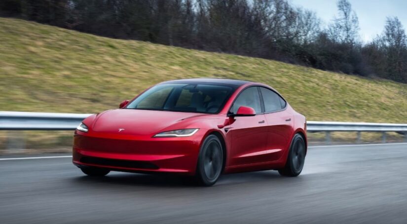A red 2025 Tesla Model 3 driving on a highway.