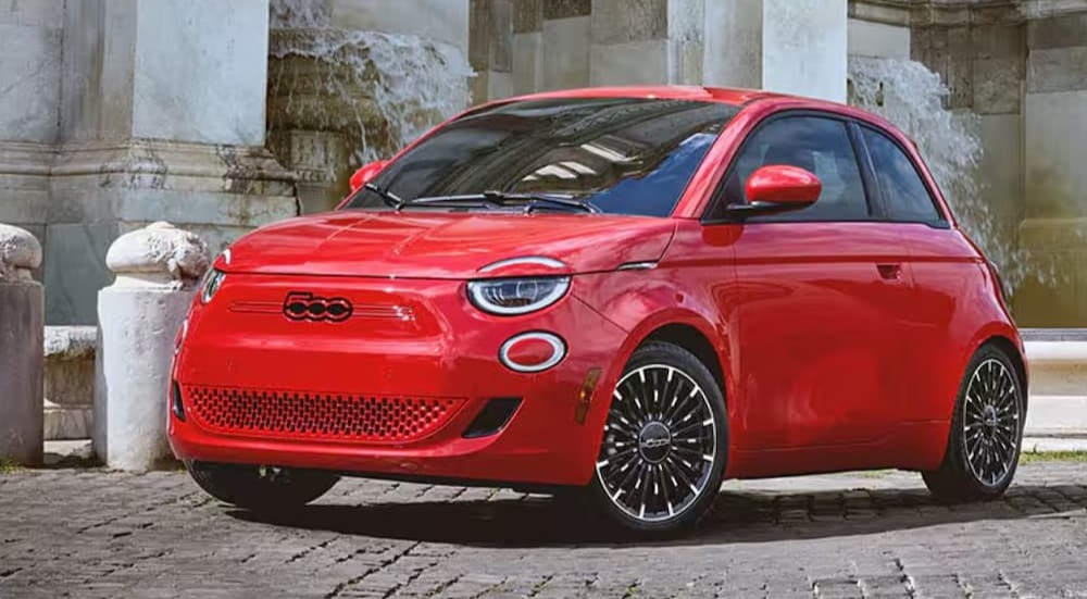 A red FIAT 500e parked near a stone building.