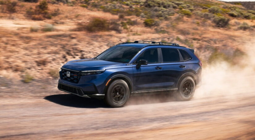 Blue 2026 Honda CR-V for sale driving down a dirt road.