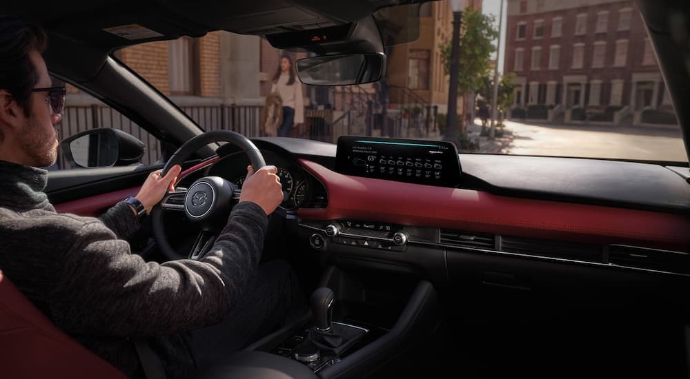 A person drives a 2026 Mazda3 down a city street.