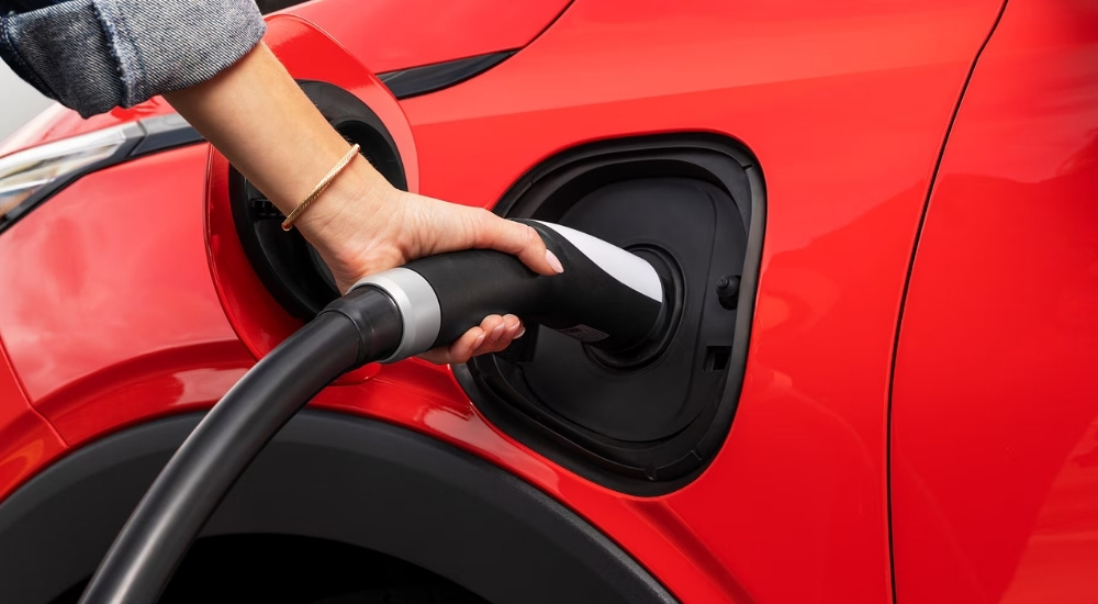 A red 2027 Chevy Bolt RS being plugged in to charge