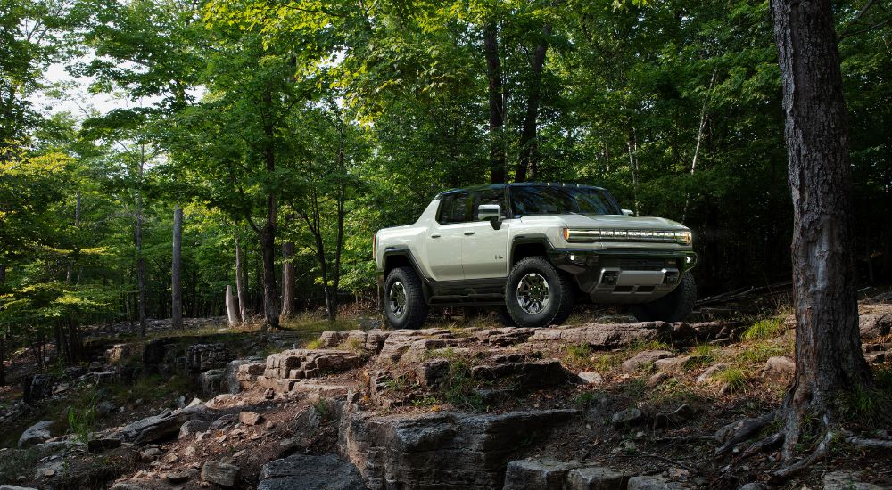 White 2023 GMC Hummer EV driving through a wooded area.
