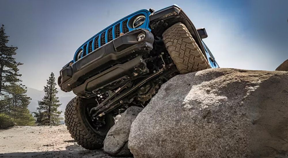 A blue 2023 Jeep Wrangler Rubicon crawling a rock.