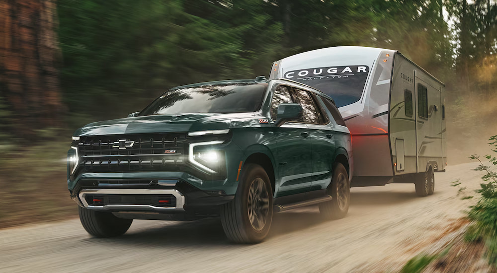 Green 2026 Chevy Tahoe Z71 towing a camper down a trail