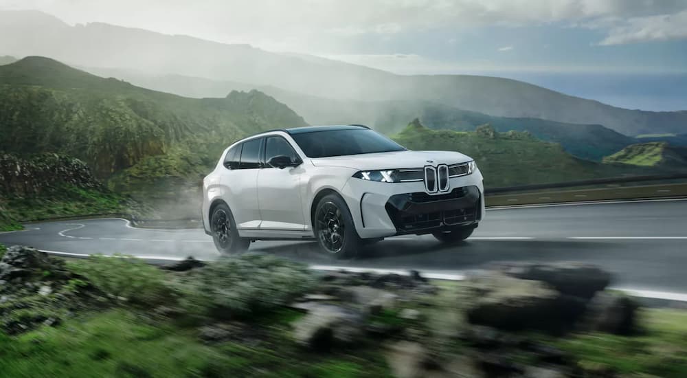 A white 2027 BMW X5 driving on a road in the mountains