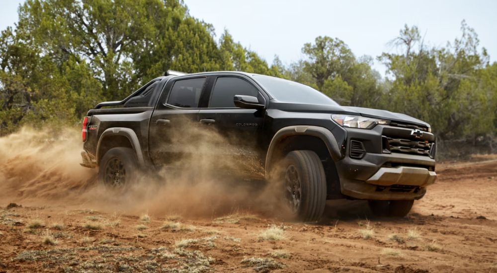 A black 2026 Chevy Colorado Trail Boss Midnight Edition driving on a dirt field.